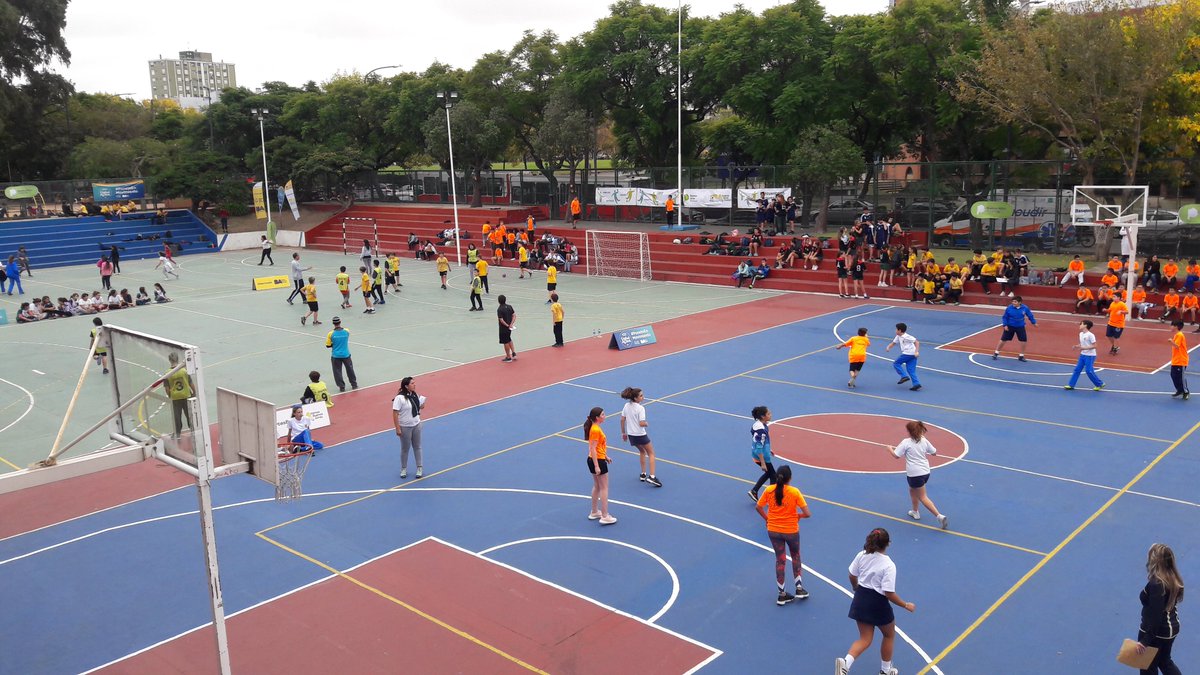 Una cancha de futbol a la derecha y una de basquet a la izquierda con adolescentes practicando deportes