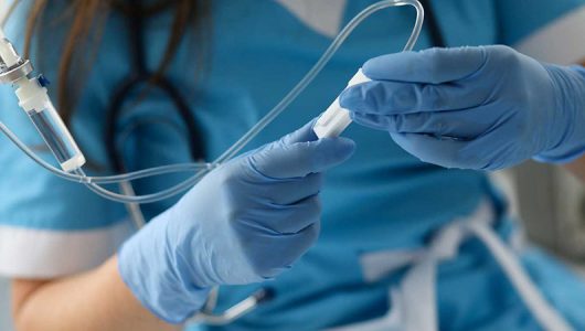 Female nurse hand in blue protective gloves hold dropper