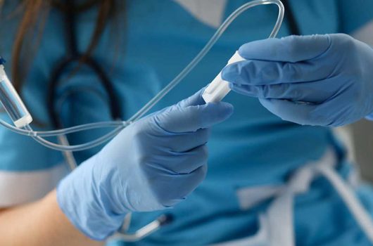 Female nurse hand in blue protective gloves hold dropper