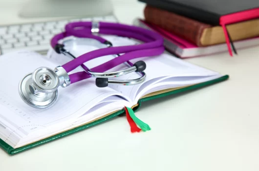 Agenda en la que se encuentra apoyado un estetoscopio y una pila de libros a la derecha
